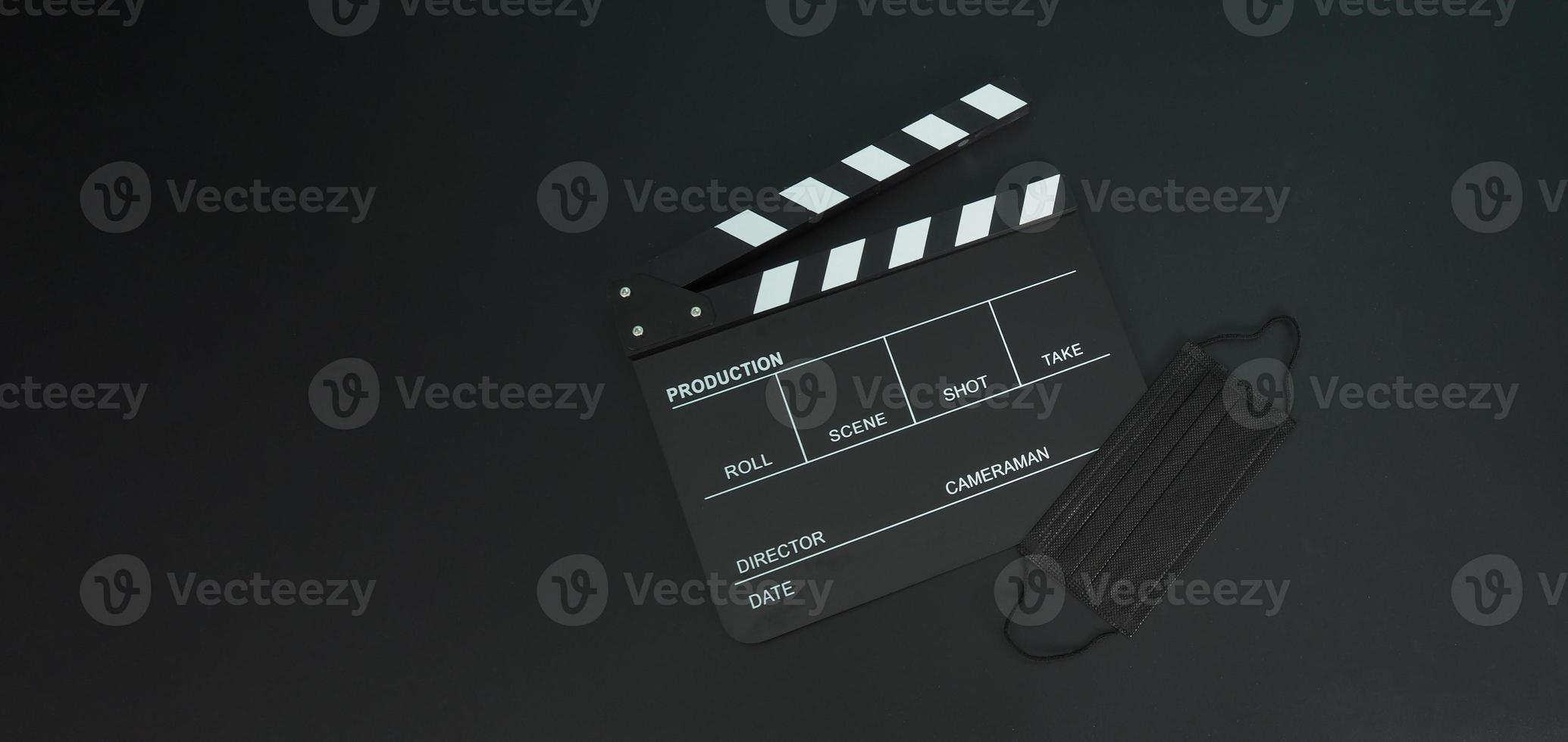 Clapper board or movie slate with black face mask or medical mask isolated on black background. photo