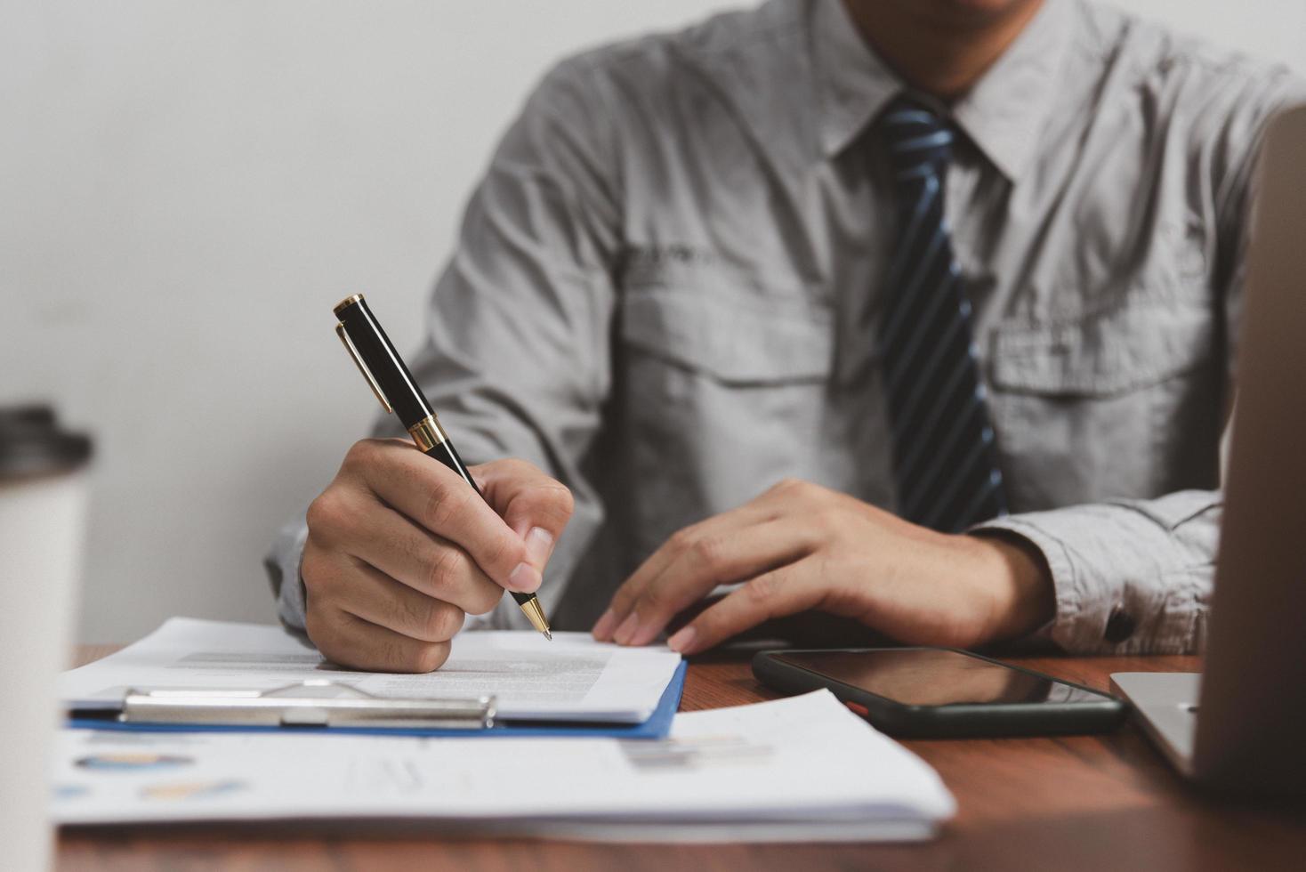 mano que sostiene la pluma que escribe papeleo documento comercial inversión financiera o contrato de firma trabajo y seguro en el escritorio. foto