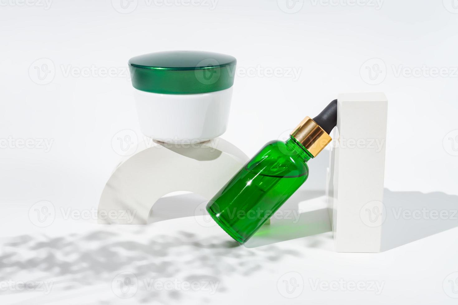 Set of green glass cosmetics bottles and cream jar on the white podium