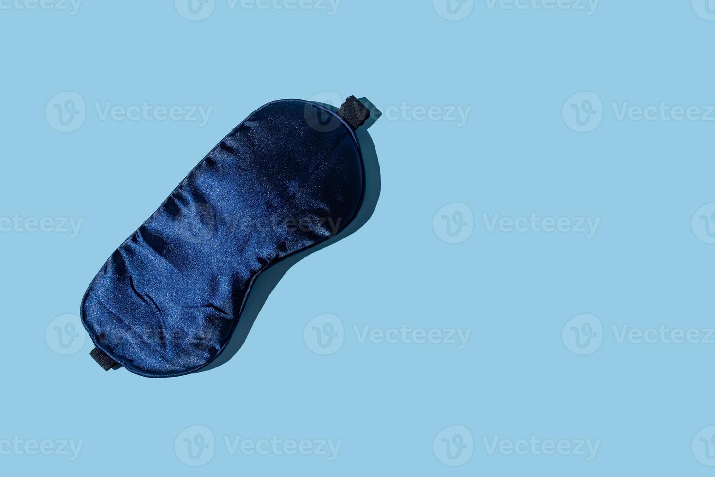 Dark blue sleeping mask on light blue background with copy space. Minimal concept of rest, quality of sleep, good night, insomnia, relaxation. Flat lay photo
