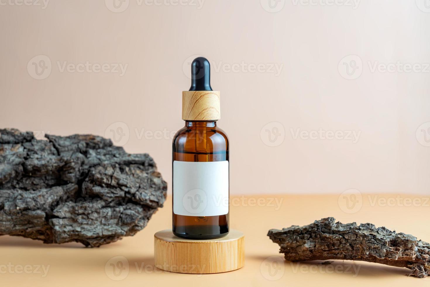 A mock-up of a brown cosmetics bottle with pipette and blank label on wooden podium with tree bark as decoration for cosmetics photography on beige background photo