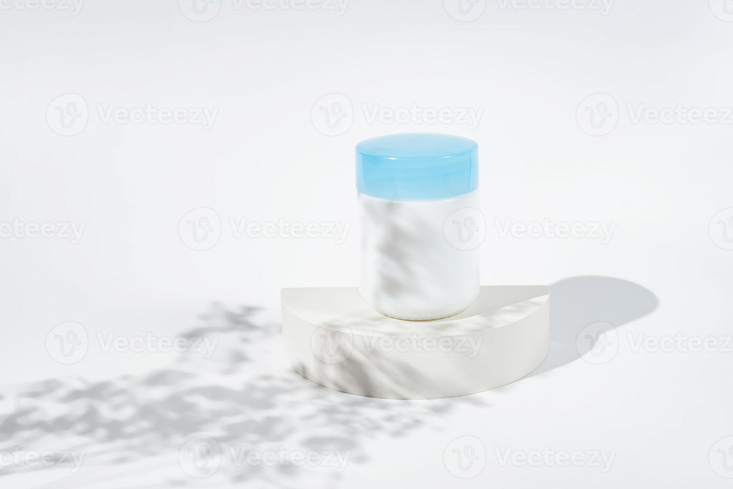 Cosmetic jar for cream on white podium and spring flowers shadows. Template for branding identity for cosmetics produce. photo