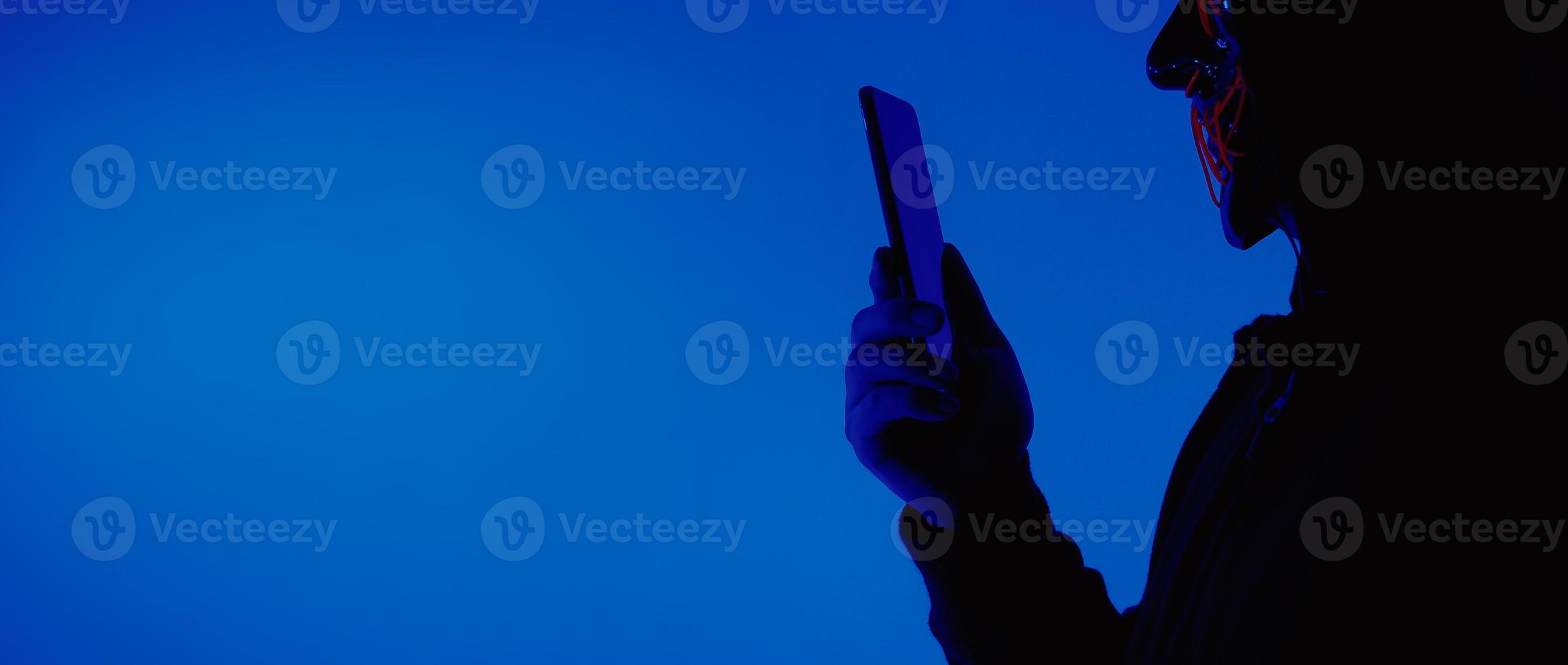 Digital security Concept. Anonymous hacker with mask holding smartphone hacked. photo