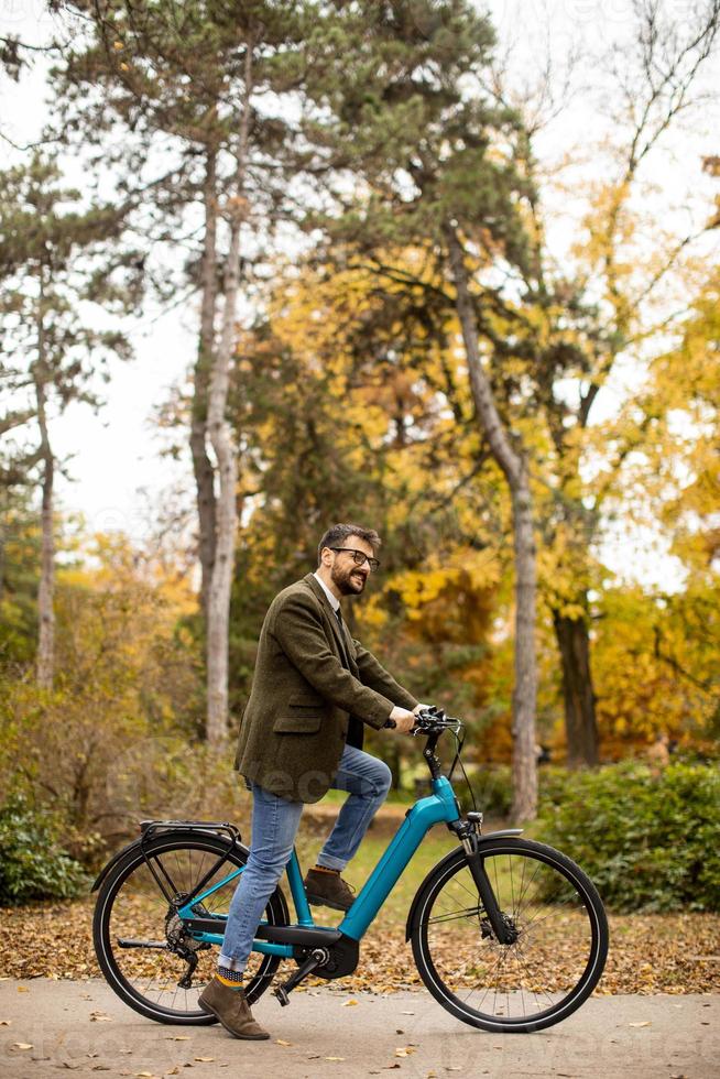 Joven con bicicleta eléctrica en el parque de otoño foto