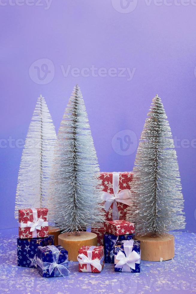 Christmas trees and gift boxes with artificial snow on purple background with copy space. photo