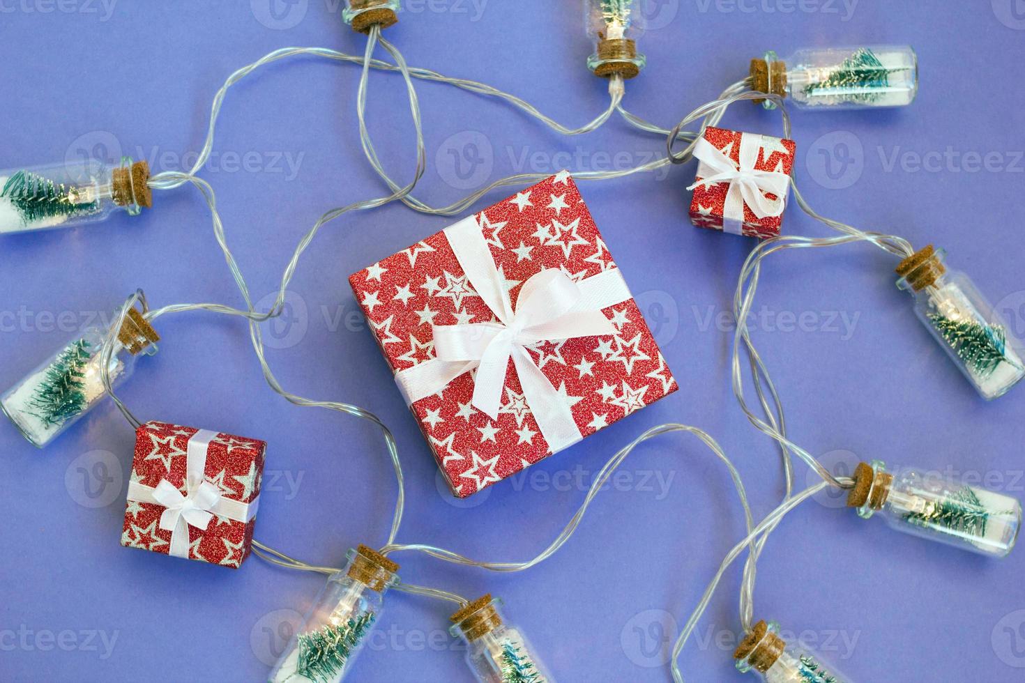 Gift boxes wrapped in red shiny paper on purple background with lights. Holiday concept for New Year or Christmas. photo