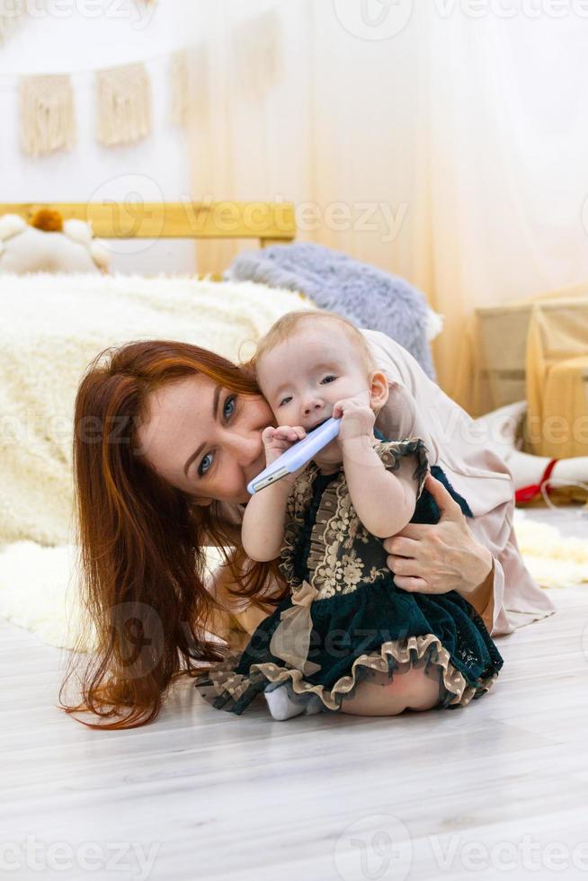 Mother and little daughter are playing with mobile phone. Happy family time at home. photo