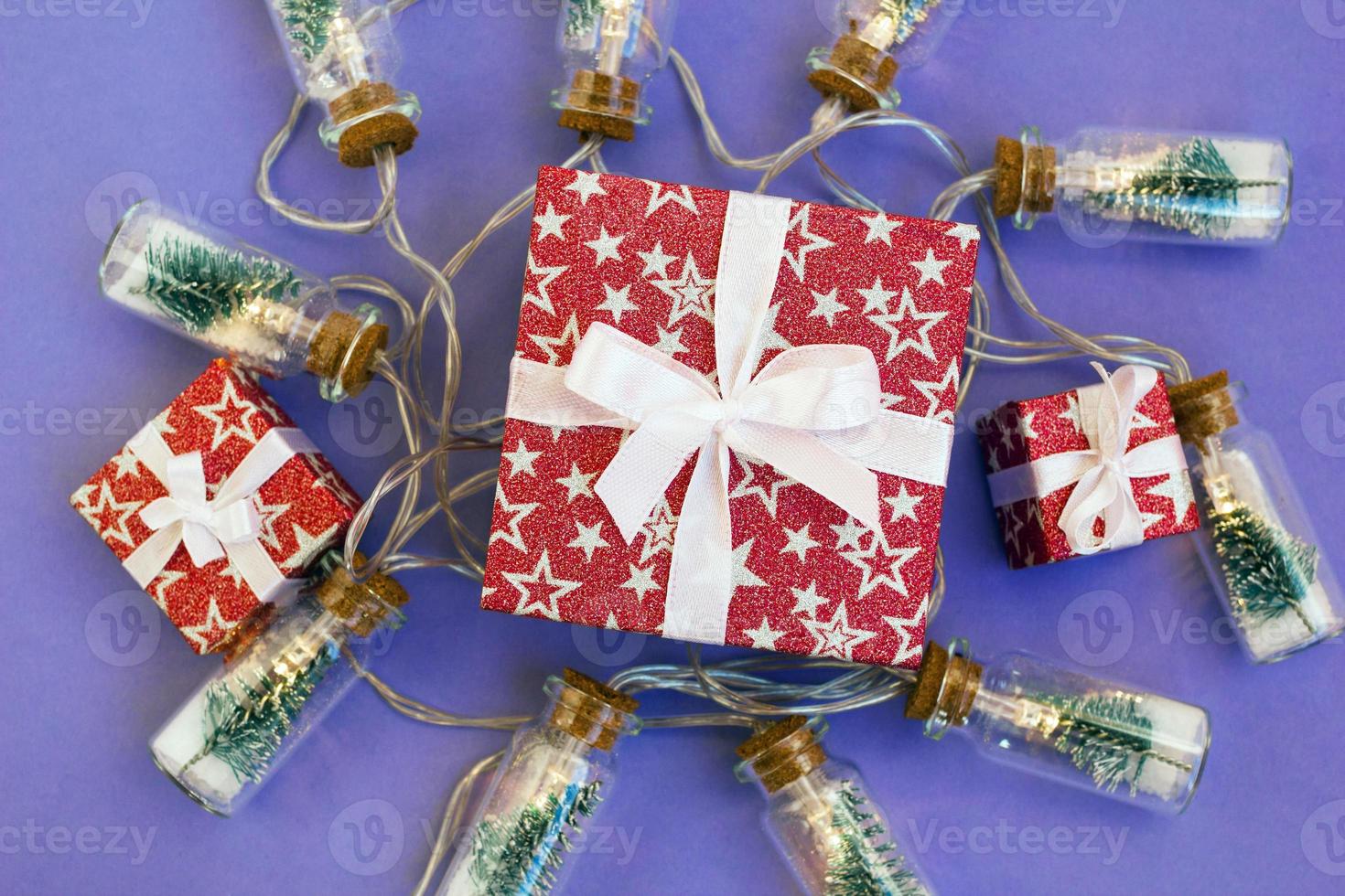 Three gift boxes in red shiny paper on purple background with Christmas lights. Holiday concept for New Year or Christmas. photo