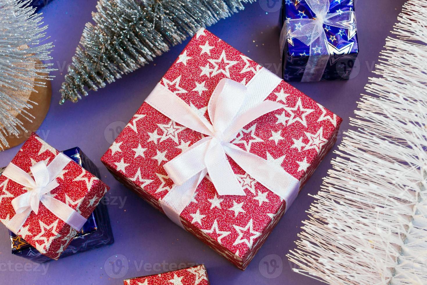 Gift boxes with shiny Christmas trees on purple background, flat lay. Holiday concept for New Year or Christmas. photo