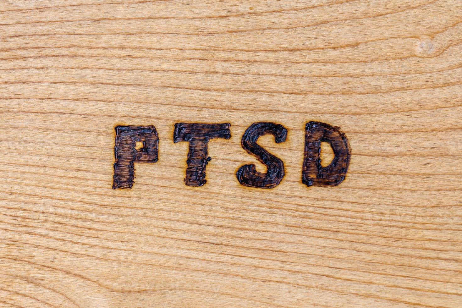 an abbreviation PTSD - post traumatic stress disorder - burned by hand on flat wooden board photo
