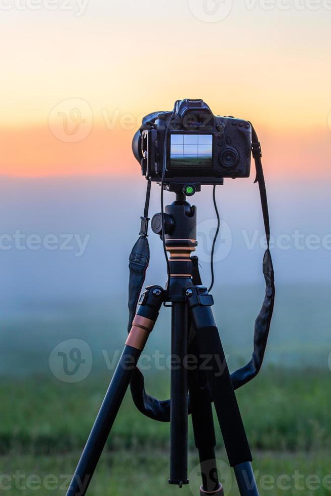 black digital camera on tripod shooting foggy morning landscape at summer with selective focus photo