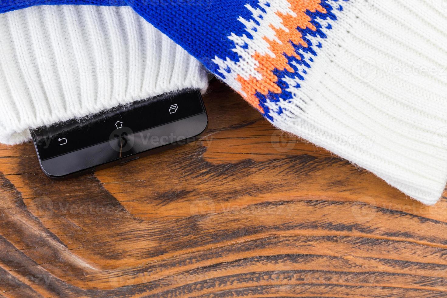 a cellphone inside blue and white knited mittens on wooden background photo