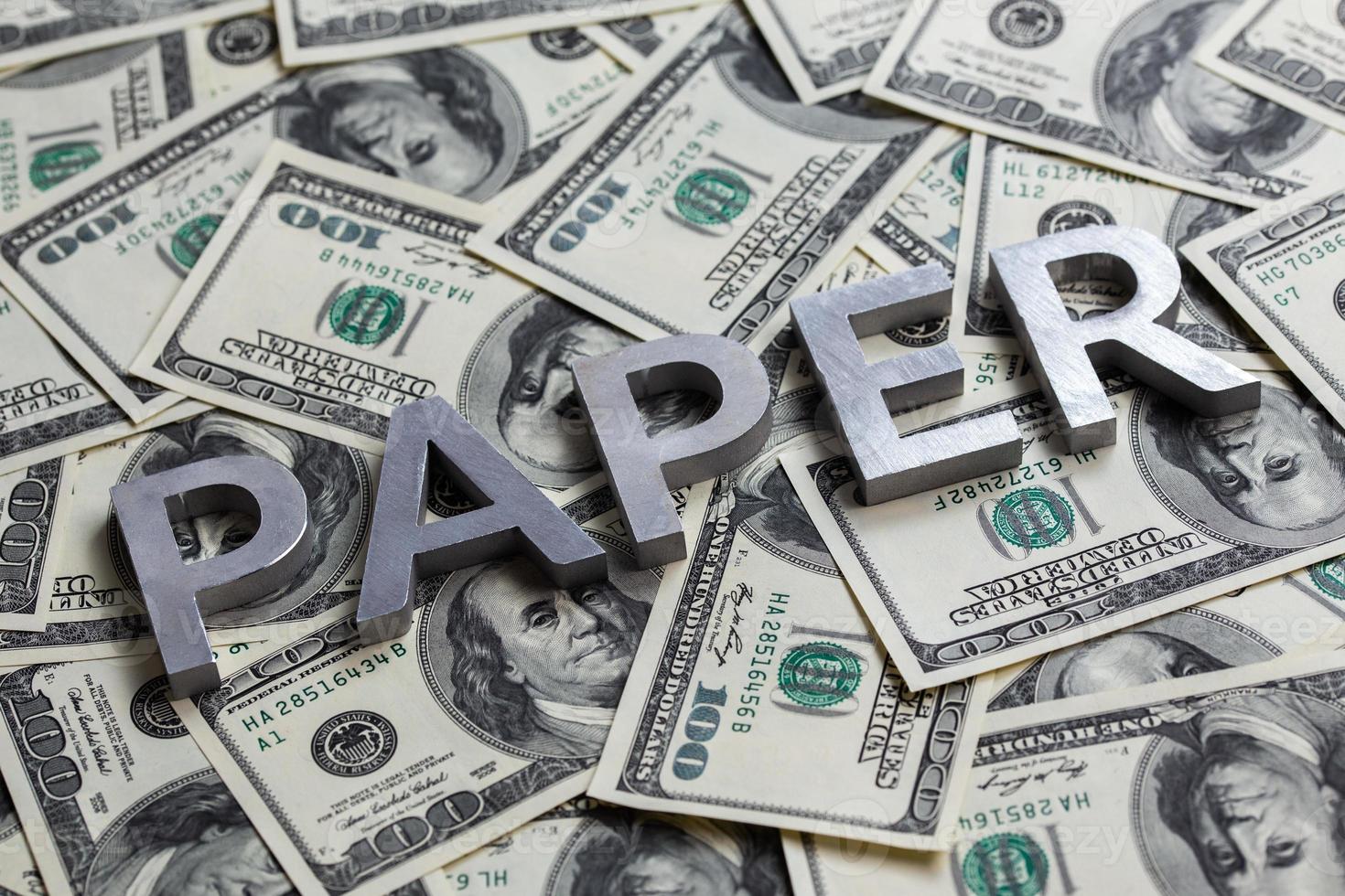 The word PAPER laid with aluminium letters on the US dollar banknotes background - with selective focus photo