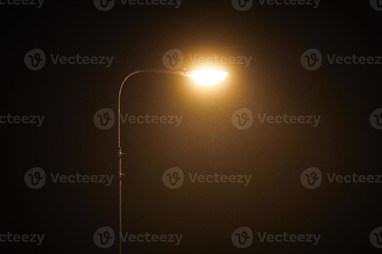 One night lamppost shines with faint mysterious yellow light through evening fog, copy space photo