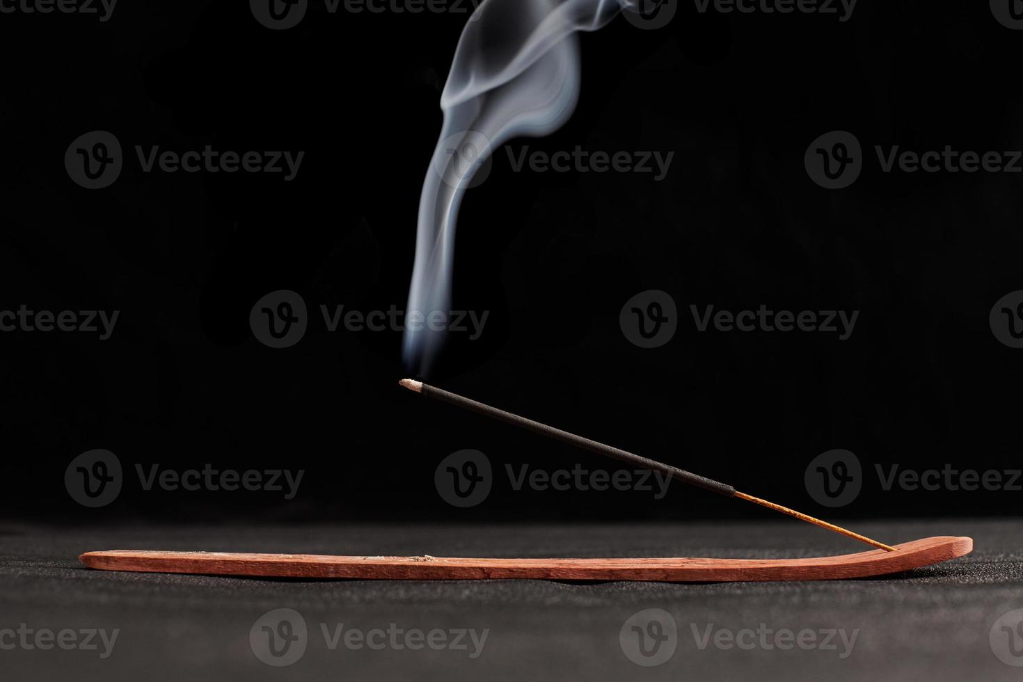 Smoke curls of burning incense stick in wooden holder for relaxation and meditation black background photo