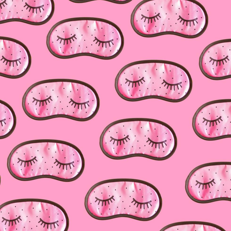 Pink sleep mask accessories for girls and young women with closed eyes on pink background pattern. Top view, flat lay. Concept of eye protection for good dreams and sleep. photo