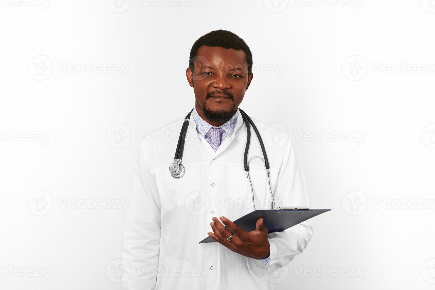 Smiling black bearded doctor man in white robe with stethoscope holds medical chart on clipboard photo