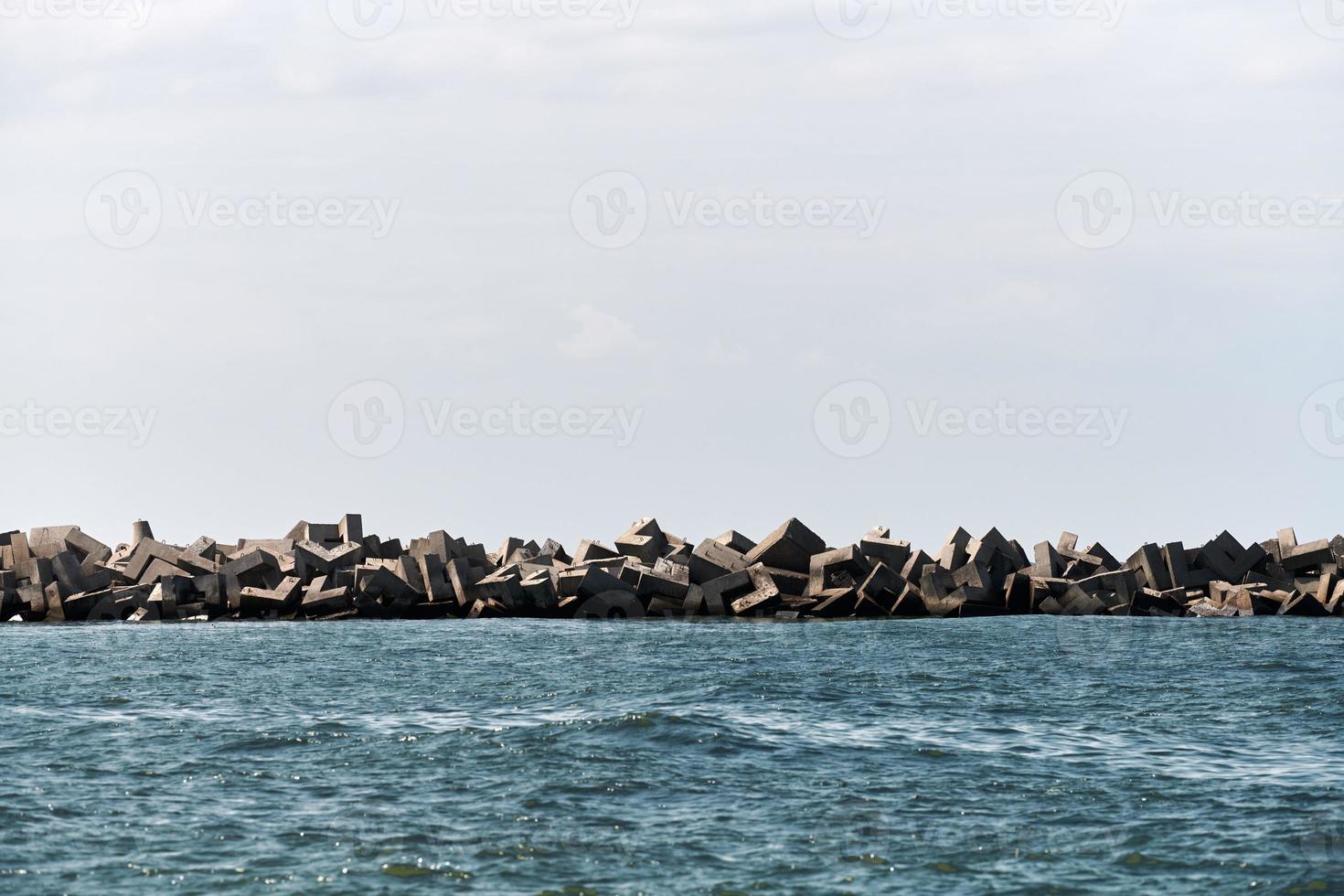 rompeolas de hormigón tetrápodos, bloques y piedras en el mar azul tranquilo, horizonte. hermoso paisaje marino foto