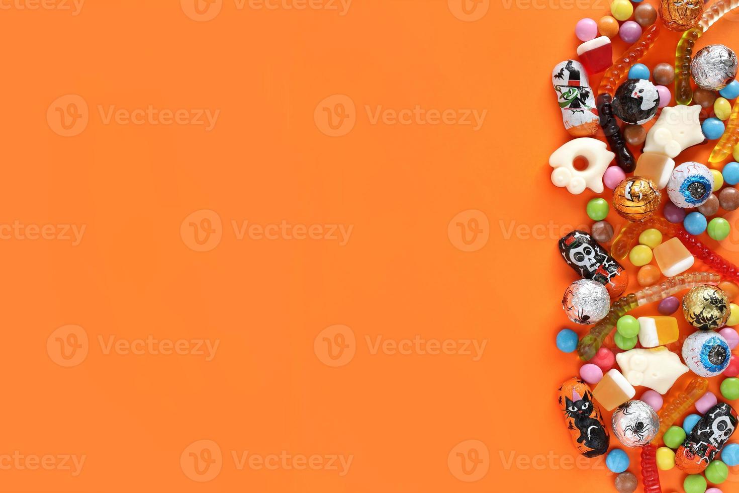 Halloween orange background with copy space on left, assorted candies on right - traditional eyeballs chocolates, jelly worms, gummy ghosts. Happy Halloween holiday sale and trick-or-treat concept. photo