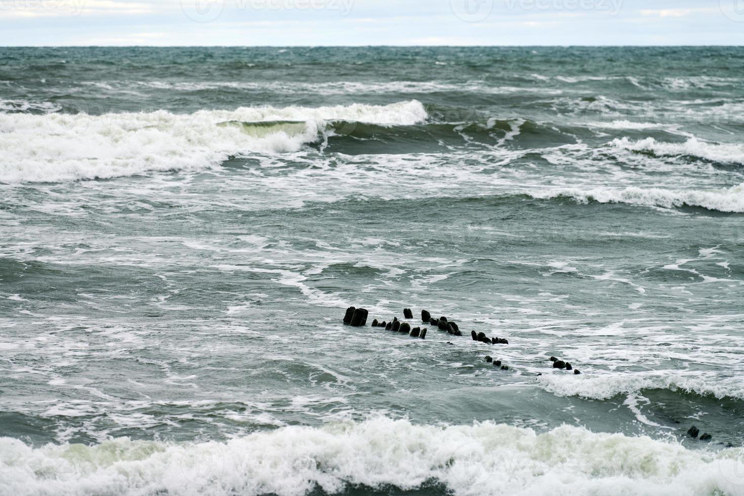 View of blue sea with foaming waves and wooden breakwaters photo