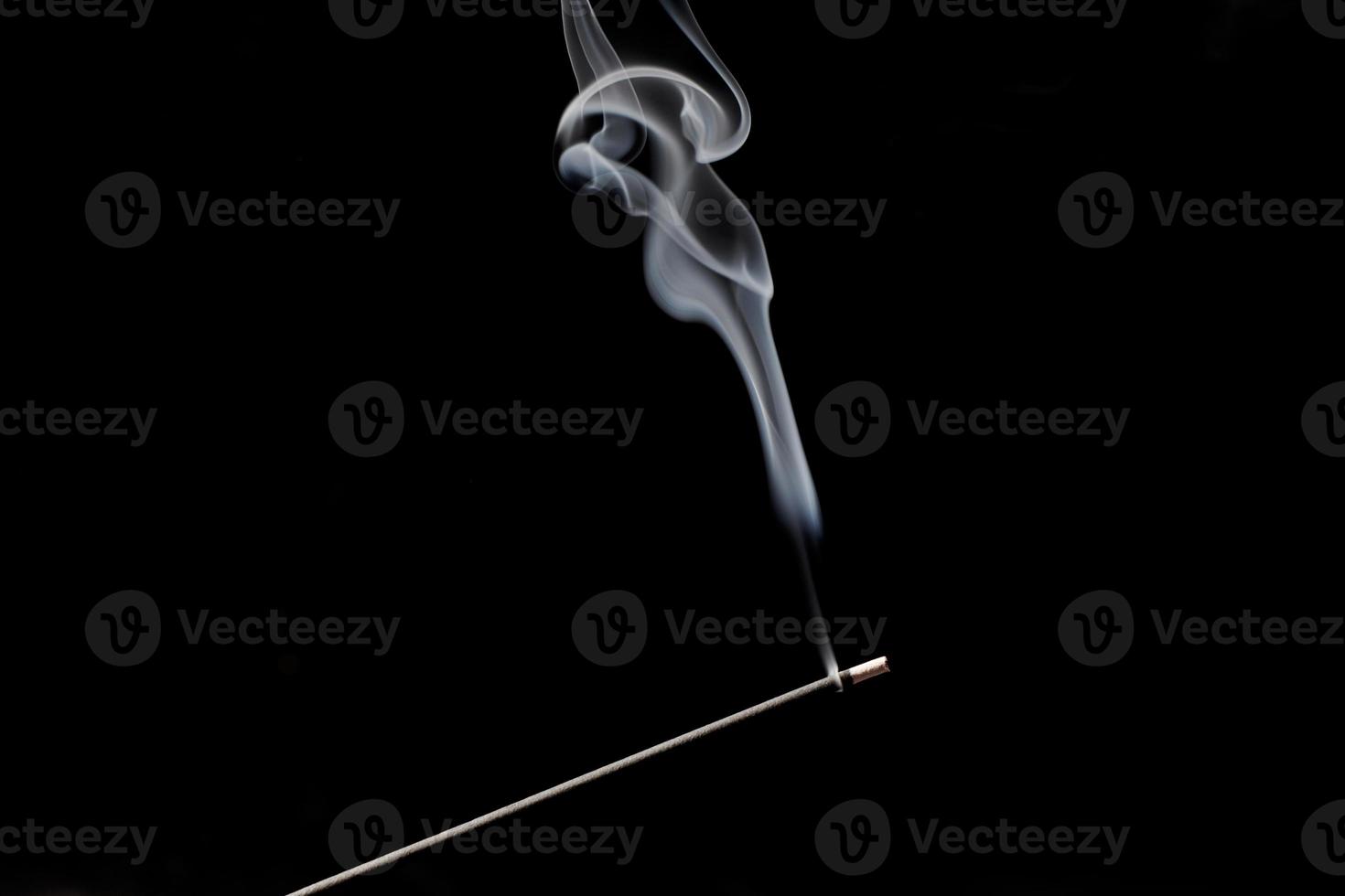 Smoke curls from burning incense stick for relaxation and meditation black background photo