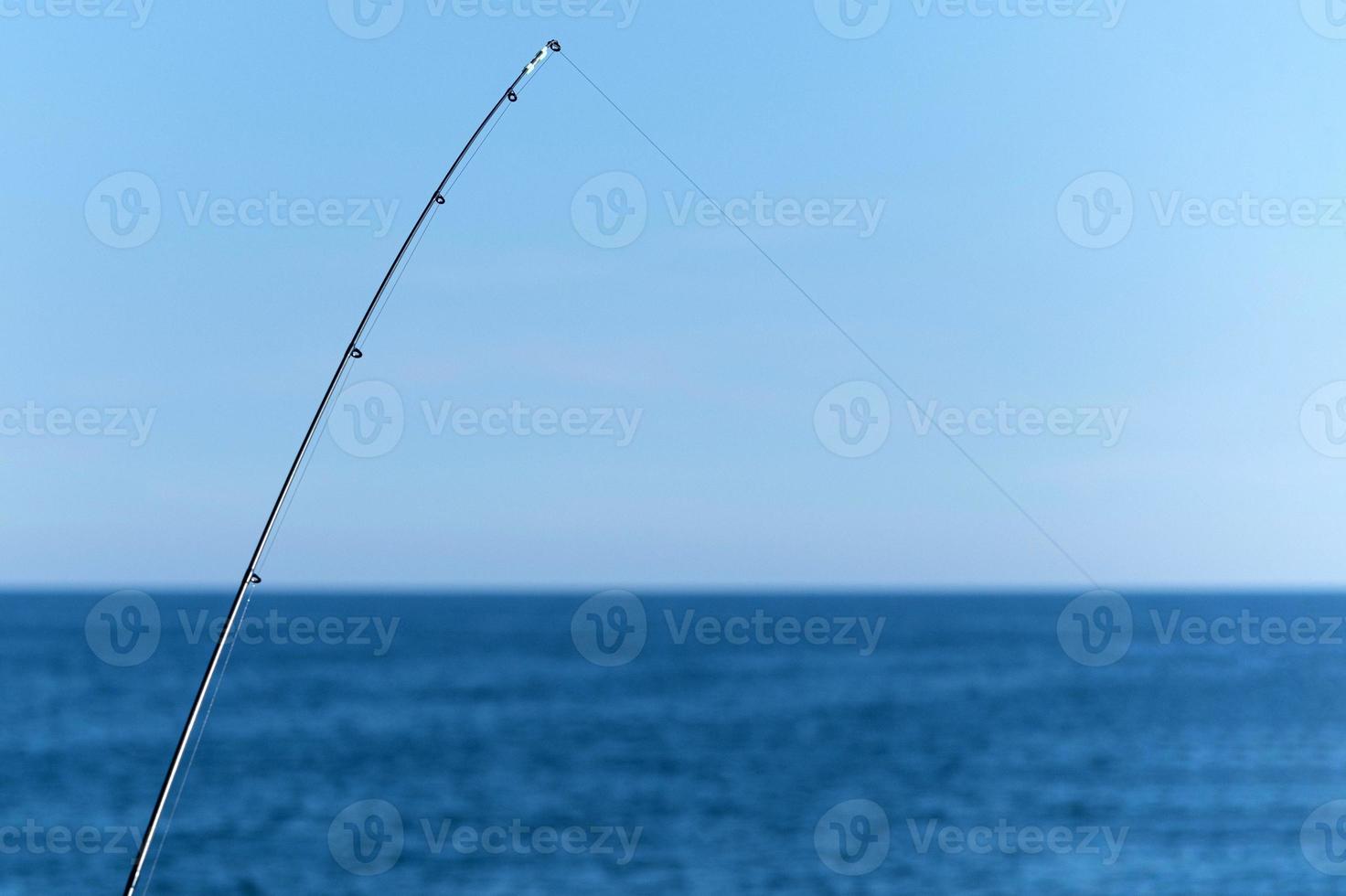 Fishing rod against blue ocean or sea background, copy space. Waiting for biggest haul. Meditative relax sport. photo