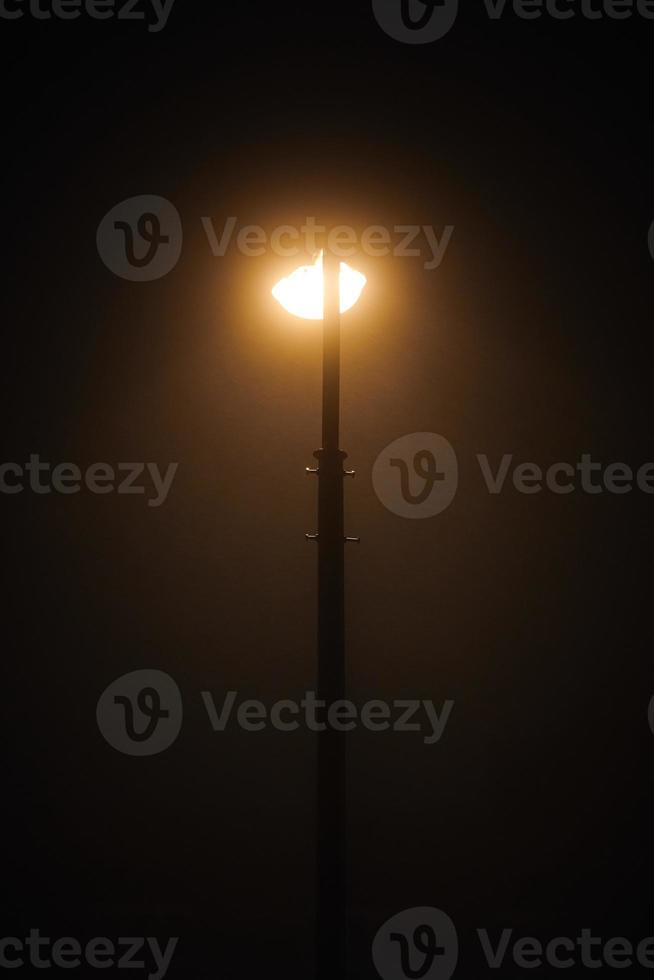 una farola nocturna brilla con una tenue y misteriosa luz amarilla a través de la niebla nocturna foto
