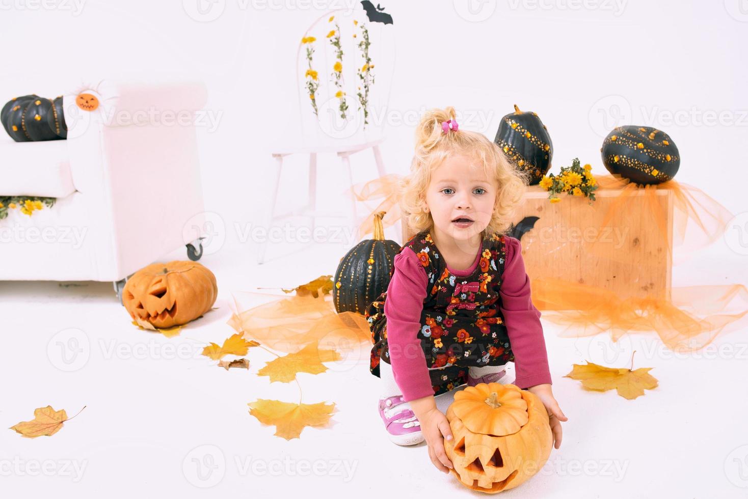 funny and cute little blonde curve girl with pumpkin in Halloween decoration photo