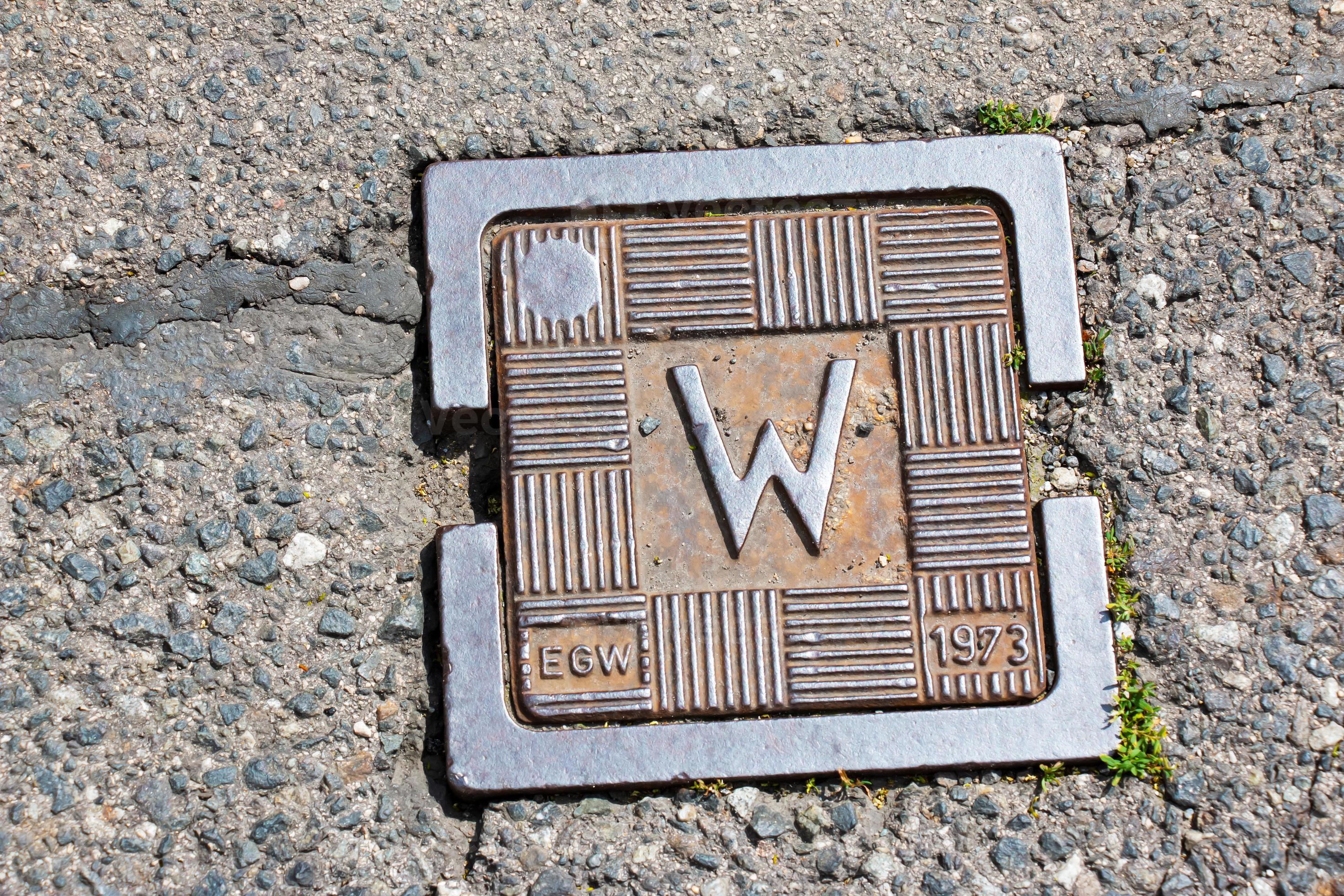 Water valve plate cover for small circular hole cap in the middle of grey asphalt 12617652 Stock