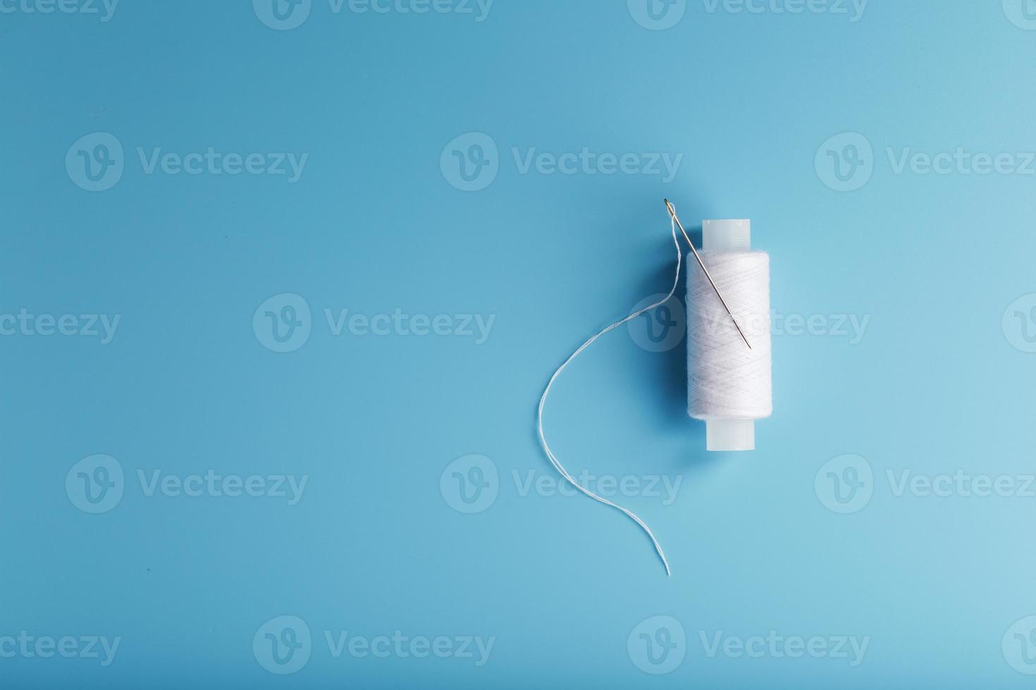 A skein of white thread with a needle on a blue background photo