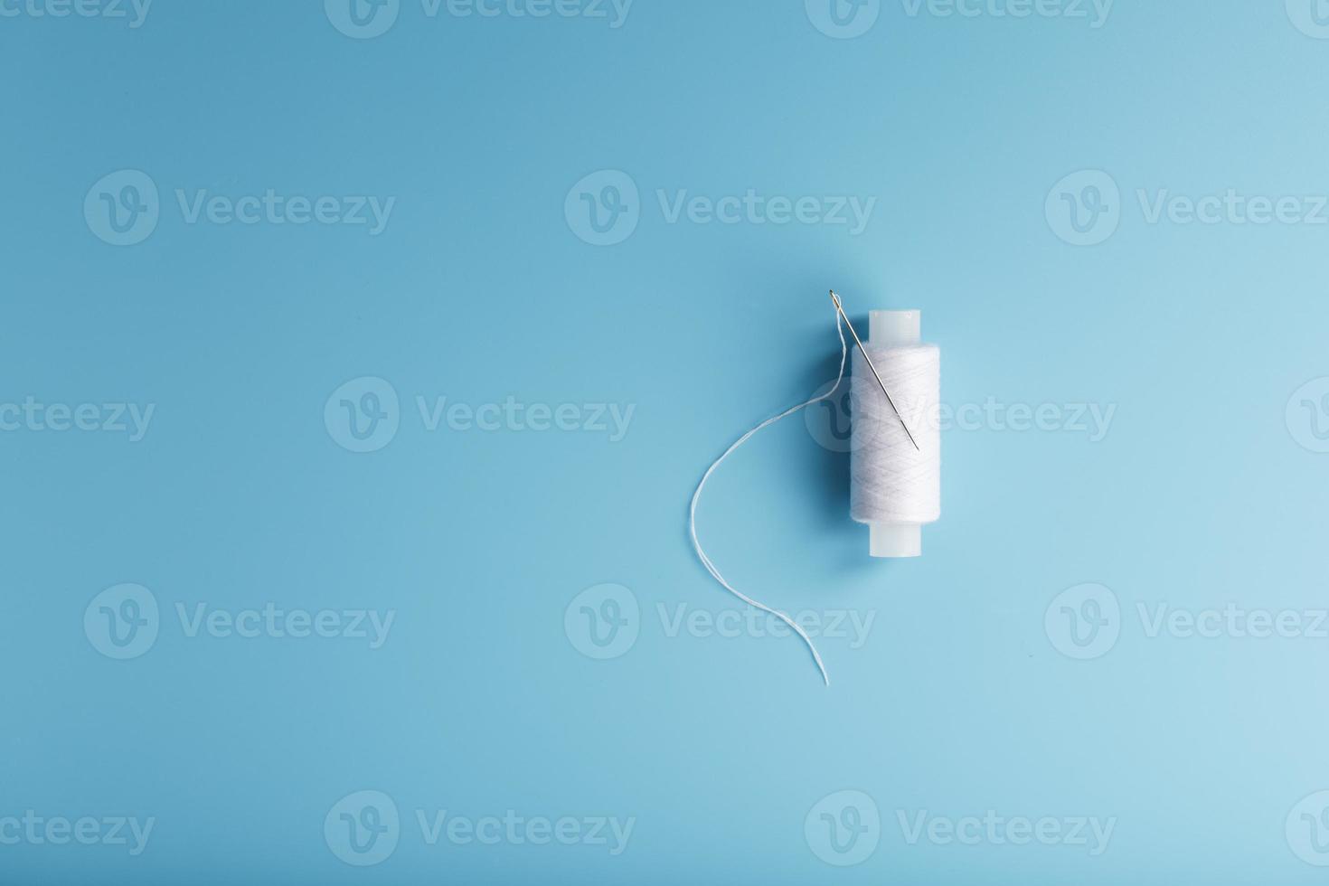 A spool of white thread with a needle on a blue background. photo