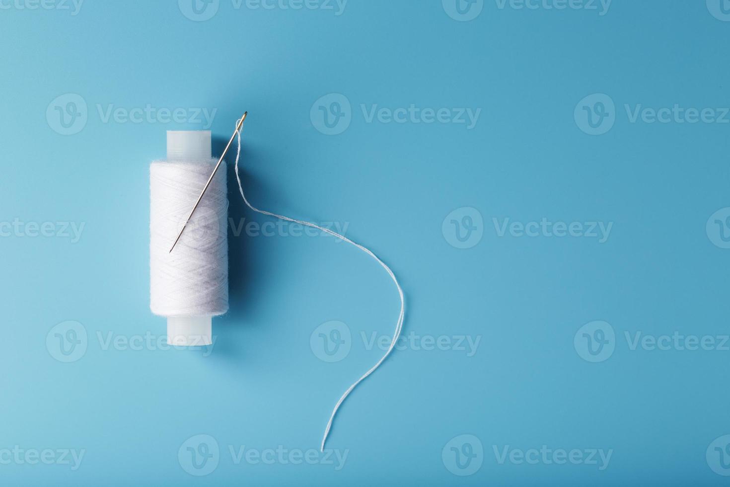 A skein of white thread with a needle on a blue background photo