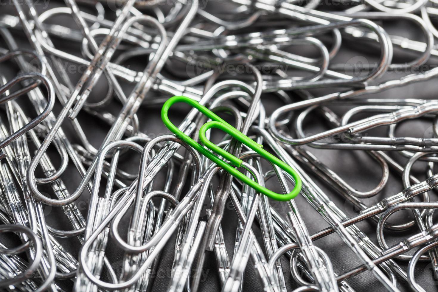 The green paper clip stands out against a textured background of silver paper clips photo