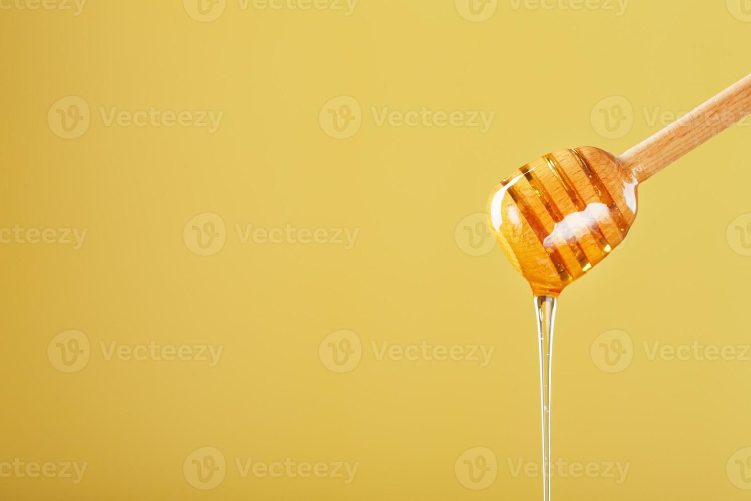 la miel dorada gotea de un cucharón de miel de madera sobre un fondo amarillo foto