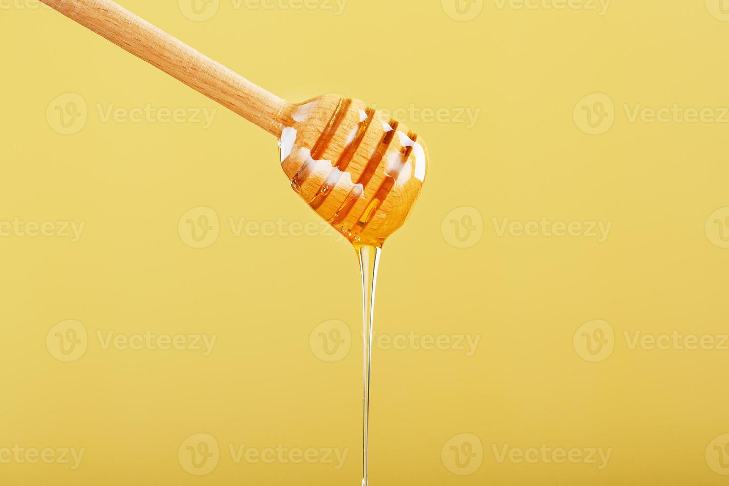 la miel gotea en una fina corriente de un cucharón de miel sobre un fondo amarillo. foto