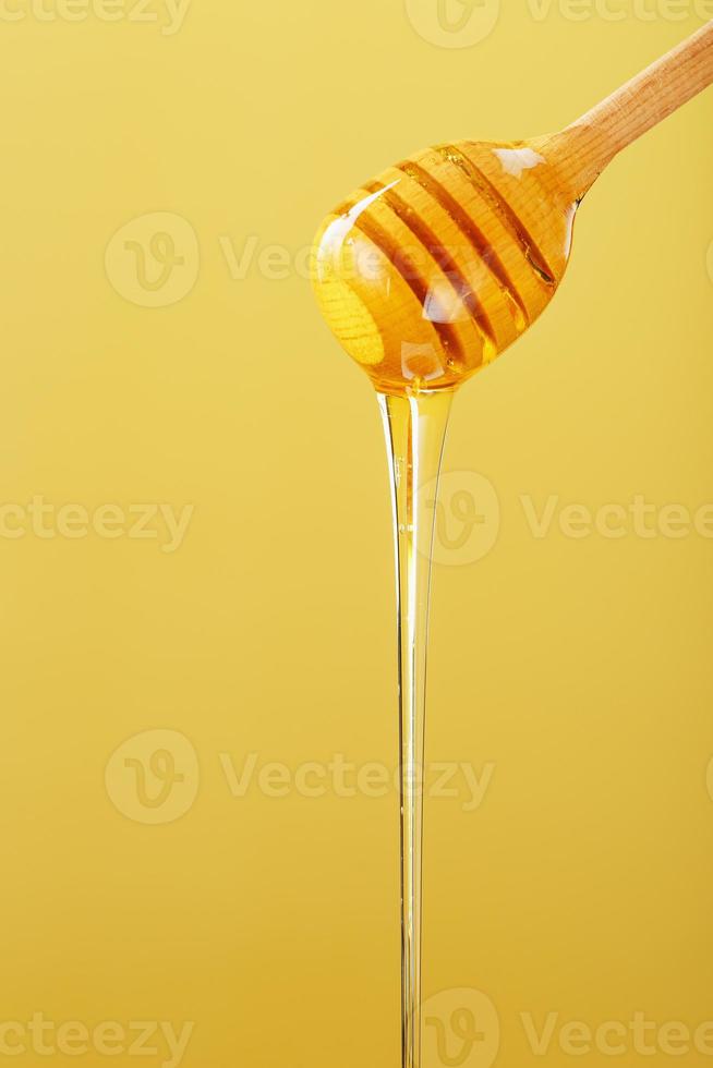la miel dorada gotea de un cucharón de miel de madera sobre un fondo amarillo foto
