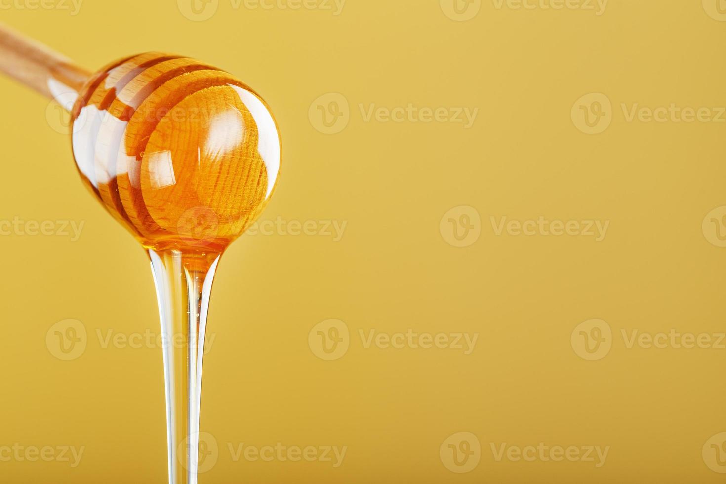 Golden honey trickles from a wooden honey dipper on a yellow background photo