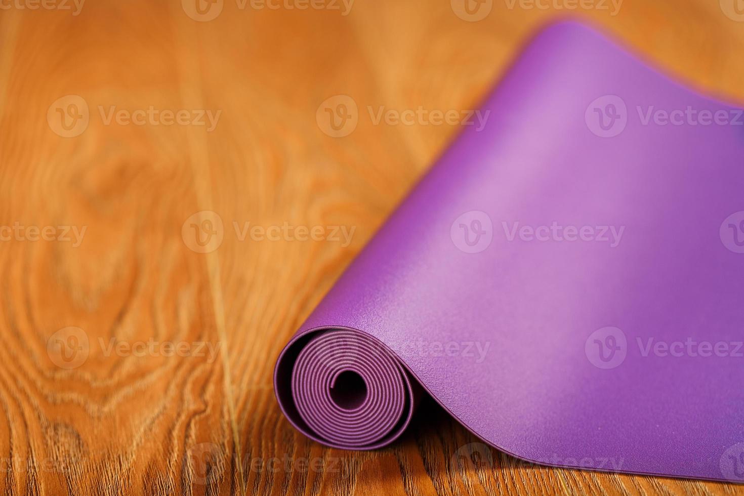 una alfombra de yoga de color lila desplegada se despliega en el suelo de madera. foto