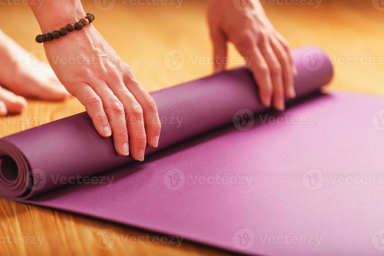 A girl lays out a lilac yoga mat before a workout practice at home on a wooden floor. photo