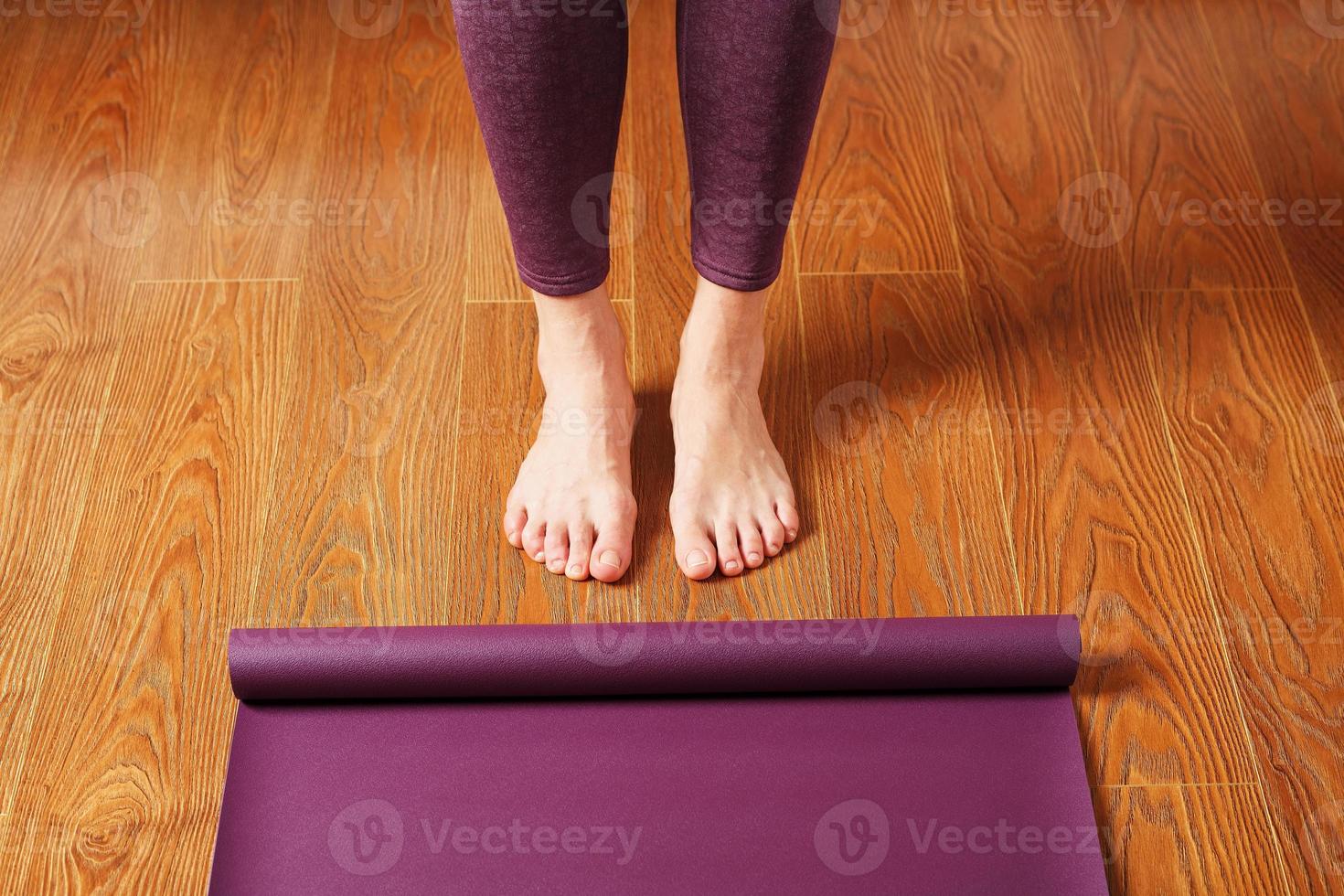 los pies de la niña se paran frente a una alfombra de yoga desplegada en el suelo de madera. foto