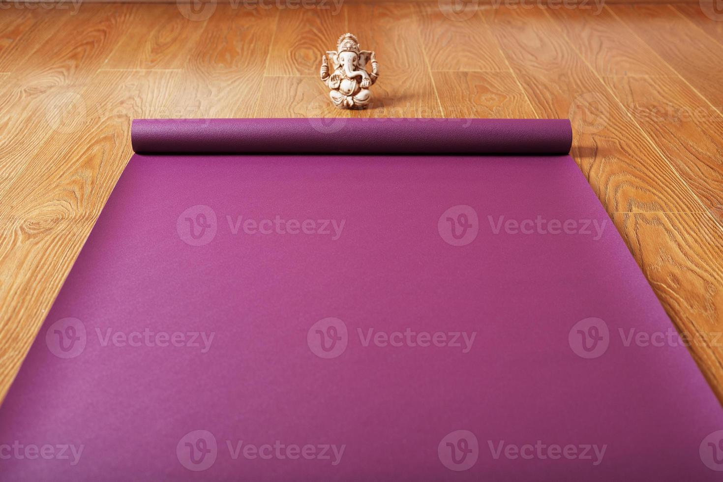 A lilac-colored yoga mat is spread out on the wooden floor with a Ganapati figurine photo