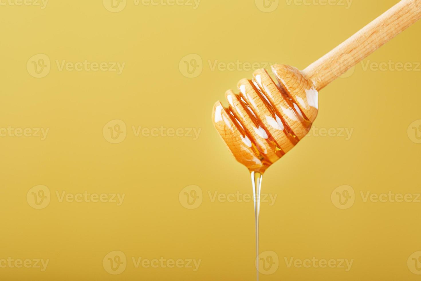 la miel gotea en una fina corriente de un cucharón de miel sobre un fondo amarillo. foto