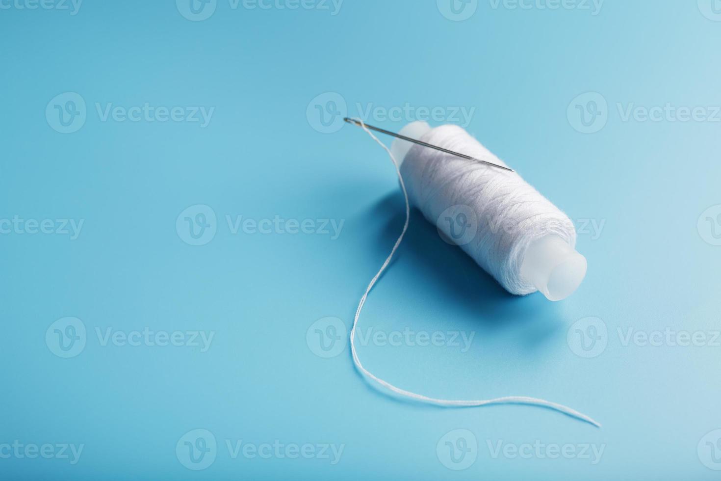 A skein of white thread with a needle on a blue background photo