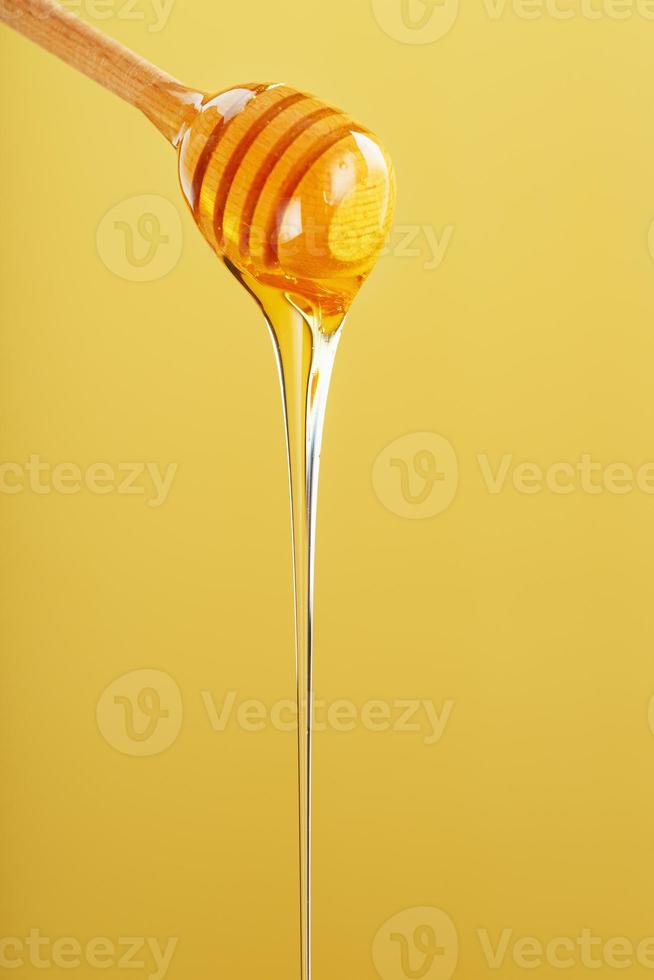 la miel gotea en una fina corriente de un cucharón de miel sobre un fondo amarillo. foto