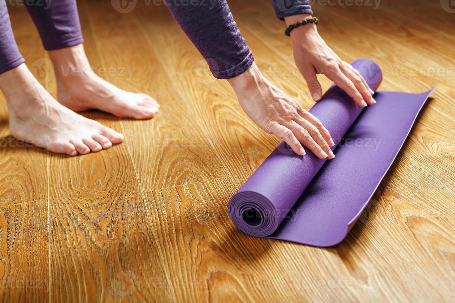 una mujer coloca una alfombra de yoga lila en el suelo de madera. foto