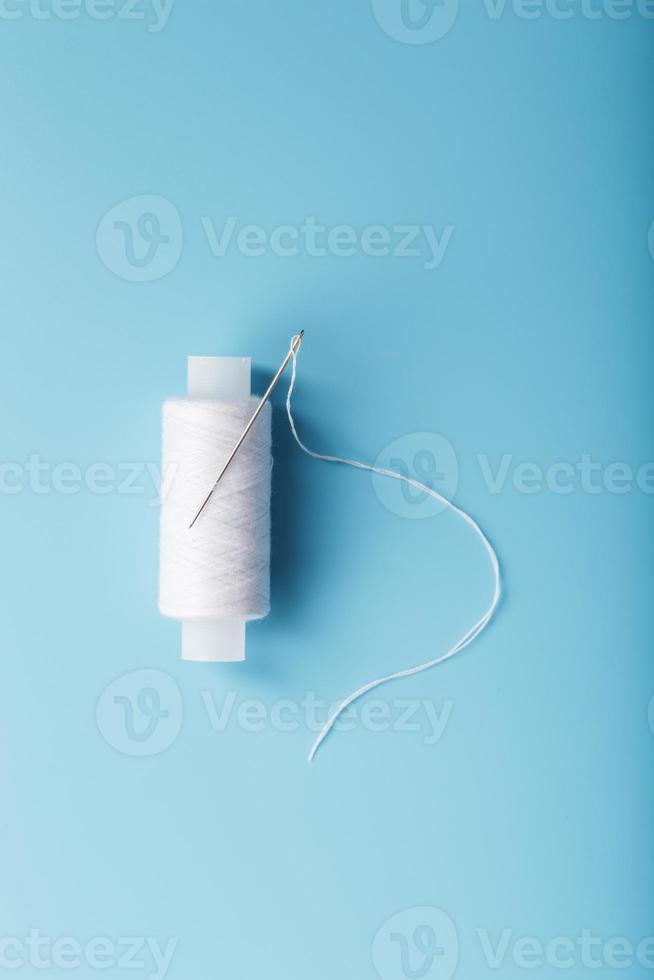 A spool of white thread with a needle on a blue background. photo