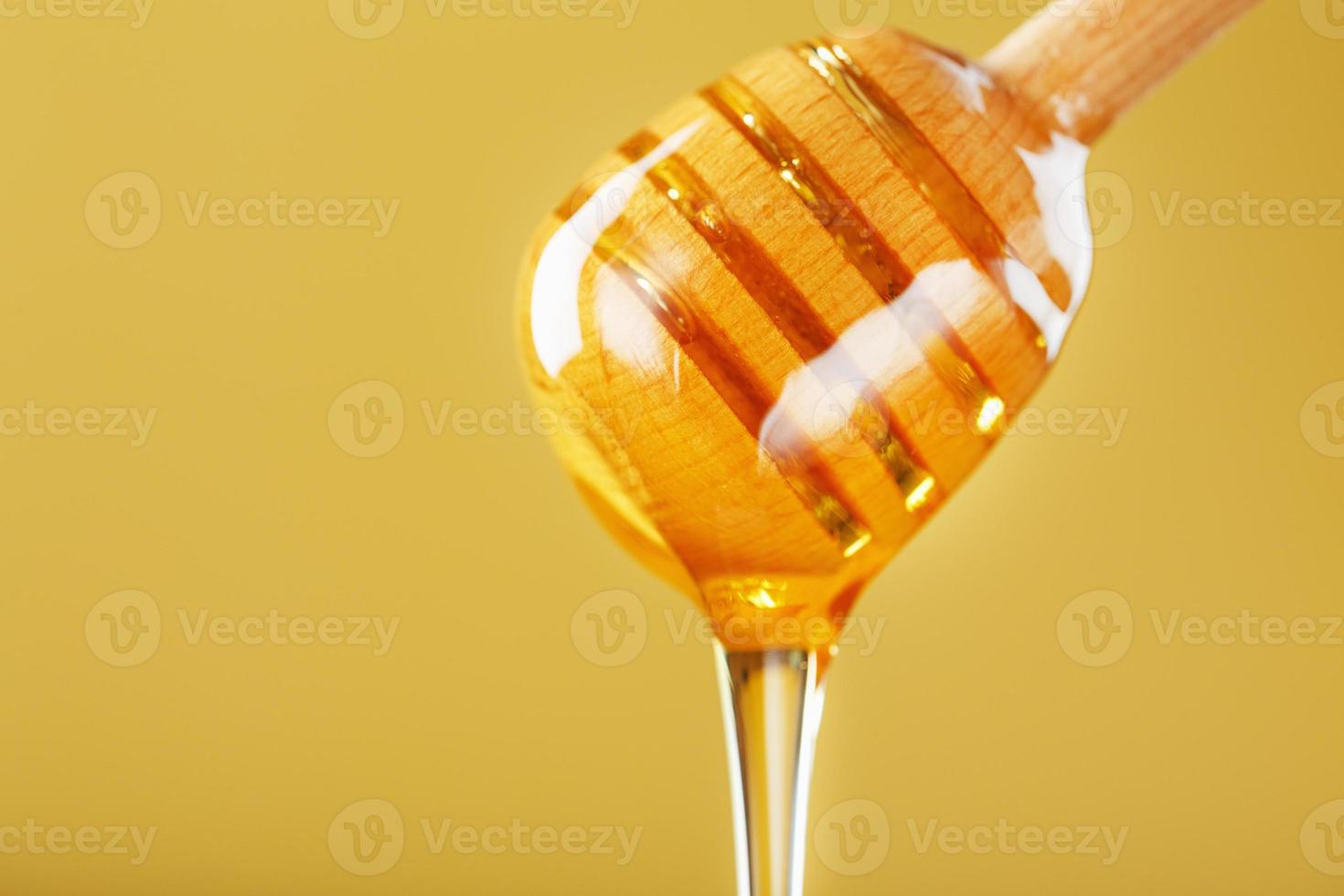 la miel dorada gotea de un cucharón de miel de madera sobre un fondo amarillo foto