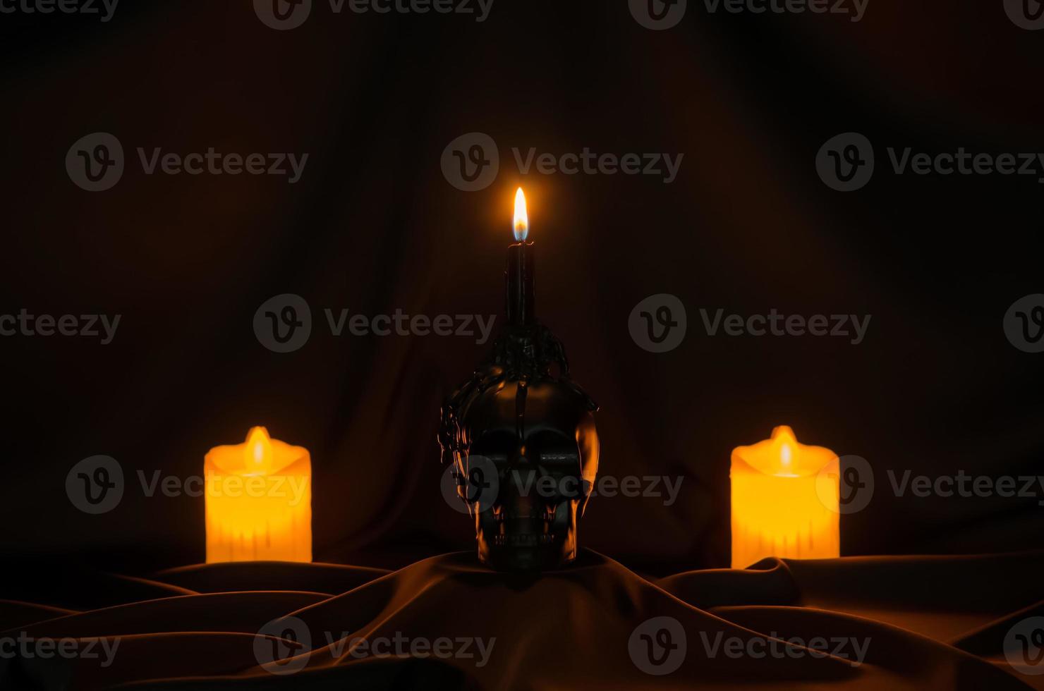 Scary halloween background with candle on skull puts on black cloth with blurred focus candles at the back. photo