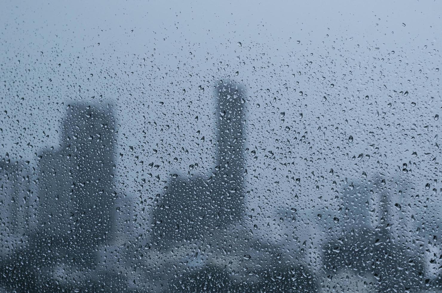 Rain drop on glass window at day time in monsoon season with blurred city buildings background. photo