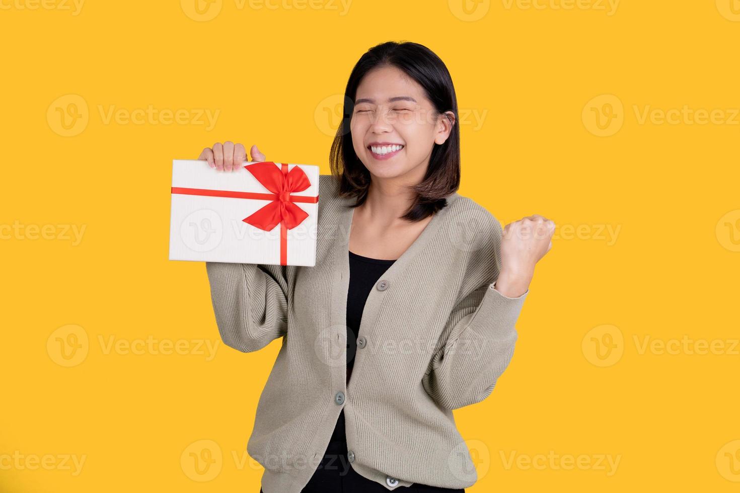 Happy Asian beautiful woman isolated on bright yellow background. She was excited about the voucher in her hand and making a winning gesture. photo